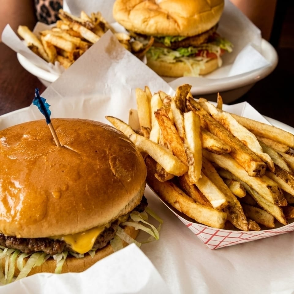 Two cheeseburgers with shredded lettuce and golden french fries on white plates.