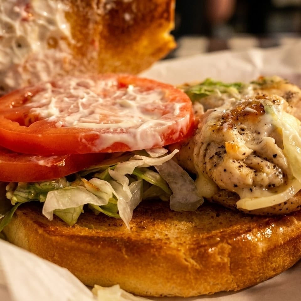 Grilled chicken sandwich with lettuce, tomato, and mayonnaise, served with red crunchy snacks.